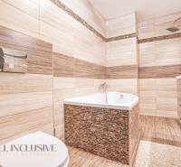 Badezimmer in einem Einfamilienhaus mit Badewanne, Dusche und Waschbecken, umgeben von beigen Fliesen.
