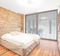Schlafzimmer mit Steinwand, bequemem Bett und erweitertem Ausblick durch das Fenster in einem Einfamilienhaus.