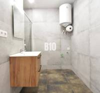 Badezimmer in einer 3-Zimmer-Wohnung mit Waschbecken und Boiler, helle Fliesen dominieren den Raum.