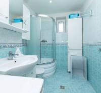 Das Badezimmer in der 2-Zimmer-Wohnung hat eine Duschkabine, ein Waschbecken, Schränke und weiße Fliesen.