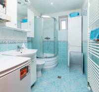 Badezimmer mit Waschmaschine und Duschkabine in einer 2-Zimmer-Wohnung. Helle Fliesen.