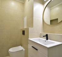 Badezimmer in einer 2-Zimmer-Wohnung mit Toilette, Waschbecken, schwarzem Wasserhahn und rundem Spiegel.