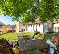 Der Garten eines Einfamilienhauses in Ploské mit einer Sitzgelegenheit unter einem Baum und Blick auf die Gebäude.