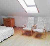 Dachzimmer mit zwei Sesseln, einer Kommode und einem Bett in einer Zweizimmerwohnung.
