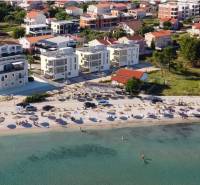 Ein Strand mit Liegestühlen und Sonnenschirmen, dahinter Häuser und Gebäude im Ferienort.