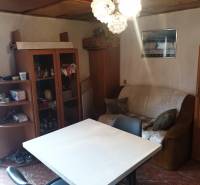 Das Innere der Hütte mit einfacher Einrichtung, einem Tisch, Stühlen und einem Sessel unter einem Kronleuchter.