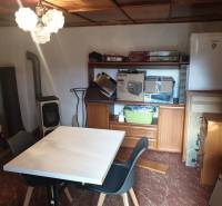 Kleiner Tisch, Stühle, Kleiderschrank, Kühlschrank, Kamin, Regale mit Gegenständen.