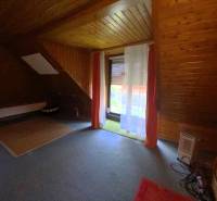 Ein Dachzimmer mit Holzverkleidung in einem Einfamilienhaus, Vorhänge über dem Fenster.