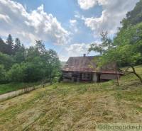 Eine Blockhütte in Zákopčí, umgeben von Wiesen und Wäldern, unter einem blauen Himmel mit Wolken.