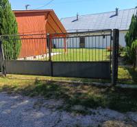 Ein Tor und eine Holzhütte in Tužina, umgeben von Rasen und Nadelbäumen.