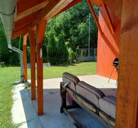 Eine Veranda bei der Hütte in Tužina mit Sitzgelegenheiten und einem Grill, umgeben von Grün.