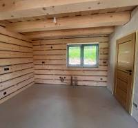 Innenraum einer Hütte mit Holzwänden, einem Fenster und einfacher Beleuchtung.