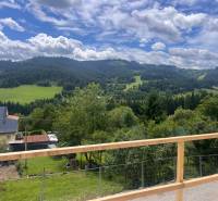 Der Ausblick von der Hütte in Korňa umfasst grüne Wiesen, Hügel und einen Himmel mit Wolken.