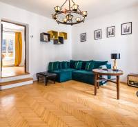 Wohnzimmer in einer 2-Zimmer-Wohnung mit Holzboden, blauem Sofa und gelben Vorhängen.
