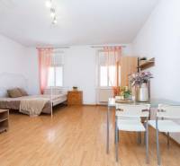 Einzimmerwohnung mit Bett, Esstisch, Holzboden und Blumendekoration.