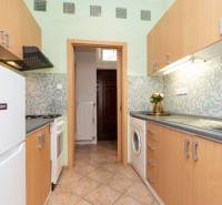 Küche in einer Einzimmerwohnung mit Holzschränken, Waschmaschine und Fliesenboden.