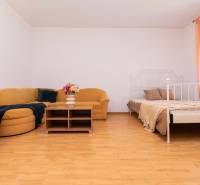 Einzimmerwohnung mit Sofa, Tisch, Bett und orangefarbenen Vorhängen am Fenster.
