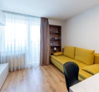 Einzimmerwohnung mit Holzboden, gelbem Sofa, Fernseher und einem Bücherregal.