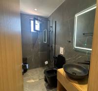 Badezimmer der Ferienwohnung mit Dusche, schwarzem Waschbecken und beleuchtetem Spiegel.