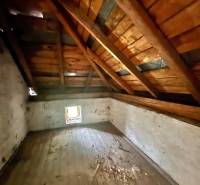 Dachbodenraum in einem Einfamilienhaus mit Holzbalkendecke und kleinem Fenster.