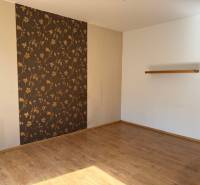 Ein leerer Raum mit Holzboden und gemusterten Tapeten in einer 3-Zimmer-Wohnung.