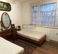 Zwei Betten, ein Spiegel, Bilder und ein Teppich im Zimmer einer Zweizimmerwohnung.