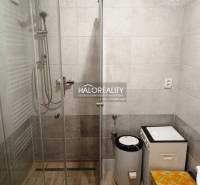 Duschkabine und Waschmaschine im Badezimmer für eine Zweizimmerwohnung mit braunen Fliesen.