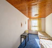 Ein Raum in einer Hütte mit einer Holzdecke, einem Tisch und Betten, Sonnenlicht und einem Teppich.