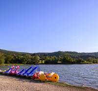 Tretboote am See in Ružiná, umgeben von Grün und Hügeln unter blauem Himmel.