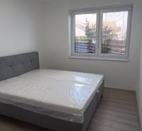 Schlafzimmer mit Bett und Fenster in einer 2-Zimmer-Wohnung, helle Wände und Boden.