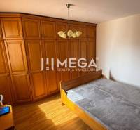 Schlafzimmer in einer 3-Zimmer-Wohnung mit einem Holzschrank, einem Bett und einem Fenster mit Jalousien.