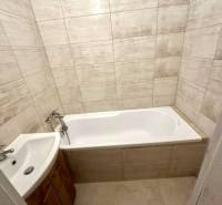 Badezimmer in einer 2-Zimmer-Wohnung mit Badewanne und Waschbecken, Fliesen in Beigetönen.