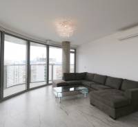 Helles Wohnzimmer in einer 3-Zimmer-Wohnung mit Ecksofa, verglasten Wänden und Blick auf die Stadt.