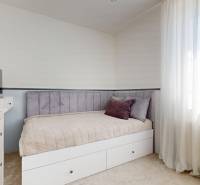 Ein Schlafzimmer im Einfamilienhaus mit hellen Möbeln, einem Fernseher und Vorhängen.