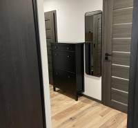 Der Flur einer 3-Zimmer-Wohnung mit Holzboden, schwarzer Kommode und Spiegel.