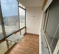 Ein verglaster Balkon einer 3-Zimmer-Wohnung mit Holzboden und Blick auf die Dächer der Gebäude.