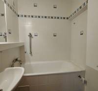 Badezimmer mit Badewanne, weißen Fliesen und Haltegriffen in einer 3-Zimmer-Wohnung.