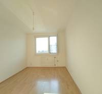 Ein leerer Raum mit einem großen Fenster, weißen Wänden und einem Boden in Holzoptik, 3-Zimmer-Wohnung.