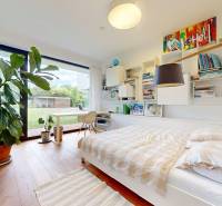 Helles Schlafzimmer in einem Einfamilienhaus mit Bett, Pflanze und Blick in den Garten.