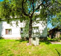 Ein Einfamilienhaus in Lúky mit einem großen Baum, einer Rasenfläche und einem Holzschuppen.