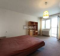 Schlafzimmer in einer Einzimmerwohnung mit Bett und Regal, helle Vorhänge.