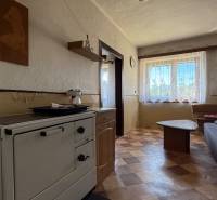 Innenraum eines Einfamilienhauses mit Küchenofen, Sofa und Tisch, Licht fällt durch das Fenster ein.