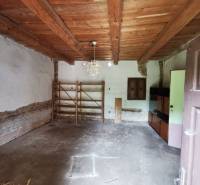 Innenraum eines Einfamilienhauses mit Holzbalkendecke, einfachem Regal und Schrank.