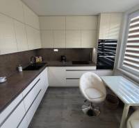 Küche in einer 3-Zimmer-Wohnung mit hellen Möbeln, Glastisch und zwei Stühlen.