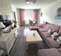 Wohnzimmer in einer 3-Zimmer-Wohnung mit rosa Sofa, Tisch und Dekorationen auf der Kommode.