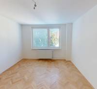 Ein Zimmer mit Parkettboden in einer hellen 2-Zimmer-Wohnung, ein Fenster mit Blick auf Bäume.