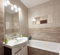 Badezimmer in einer 2-Zimmer-Wohnung mit Badewanne und Waschbecken, helle Fliesen, Spiegel.