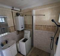 Badezimmer in einer 2-Zimmer-Wohnung mit Dusche, Waschmaschine, Waschbecken und Boiler.