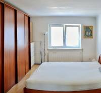 Schlafzimmer mit einem Holzbett und einem Schrank in einer 2-Zimmer-Wohnung, ergänzt durch ein Fenster und ein Bild.