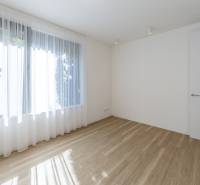 Helles Zimmer in einer 3-Zimmer-Wohnung, Holzboden, großes Fenster mit weißen Vorhängen.